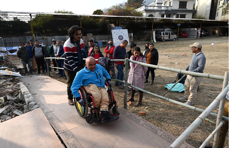 Deepak Khatri Chhetri along with a volunteer accessing a ramp. A group of participants stand around him