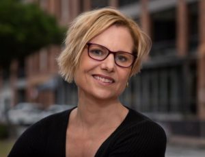 A blond woman with a short haircut wearing glasses in a black jacket